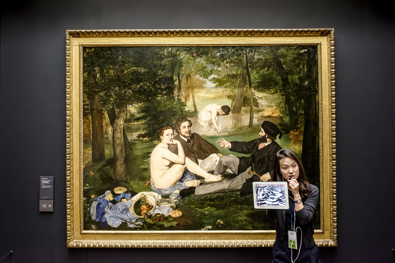 Guía explicando El Almuerzo sobre la hierba de Manet con una tablet